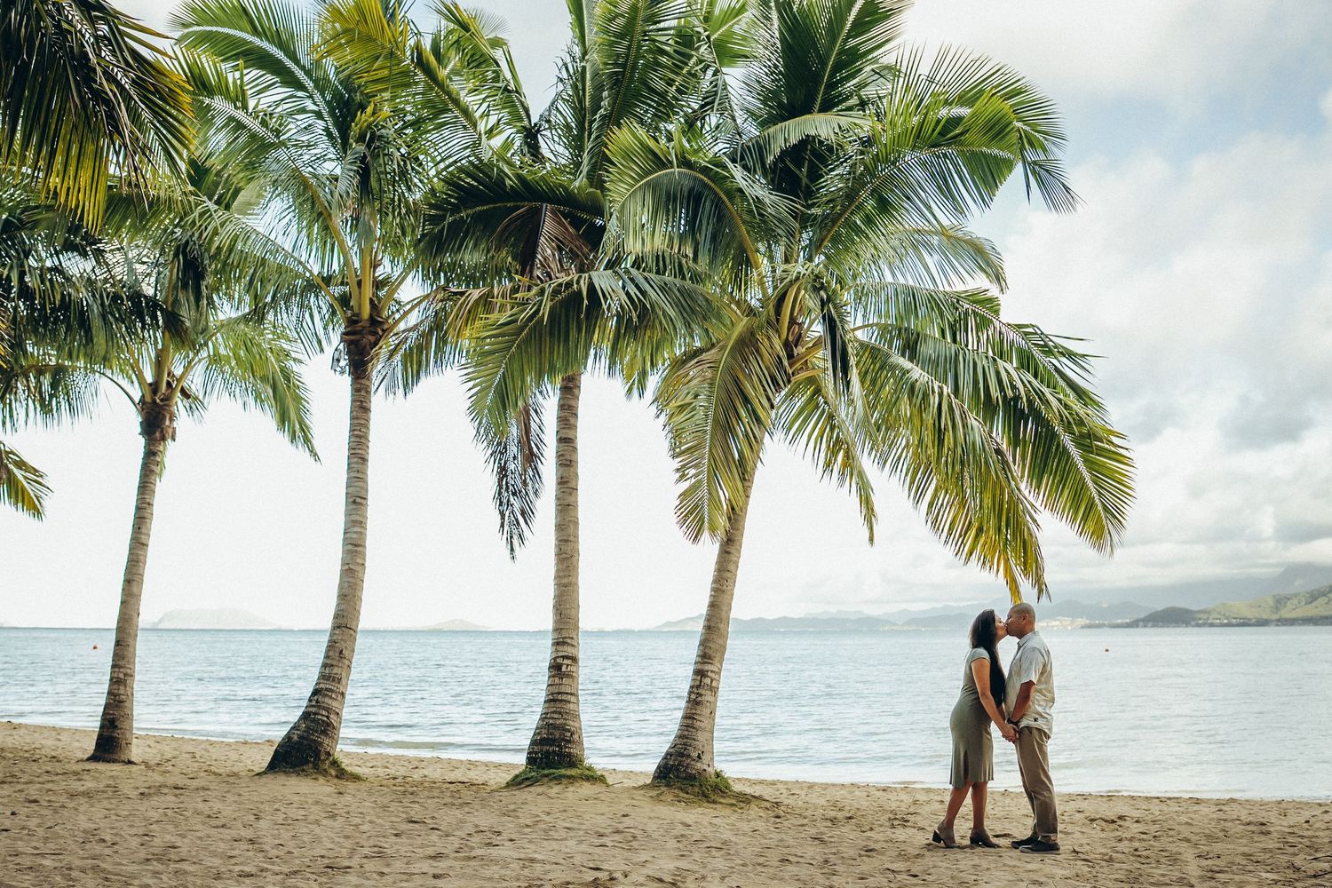 Family photoshoot at Secret Beach. A couple standing under tall palm trees on the coast of Oahu near Kualoa Ranch. Epic view