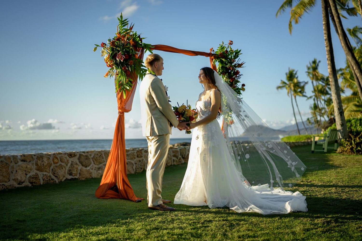 An elegant outdoor ceremony at a premier Ko Olina venue. The couple exchanges vows under a floral arch adorned with tropical blooms, framed