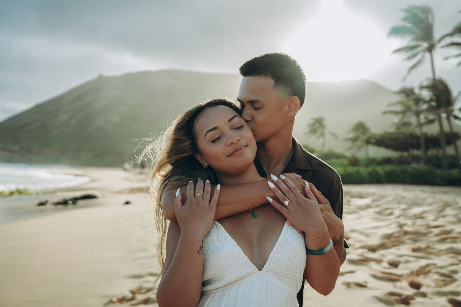 Couple embracing on a tropical beach with mountains and palm trees in the background at Sandy beach Oahu Hawaii