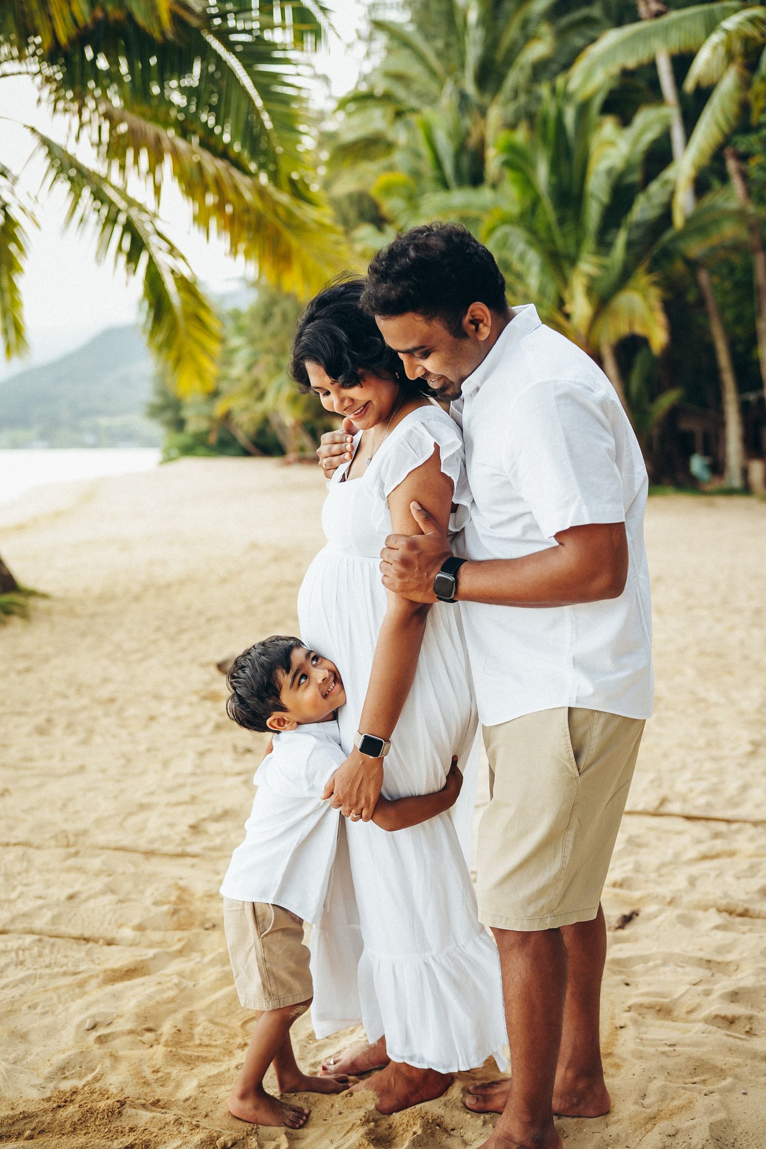 Secret Beach family photoshoot in Oahu. Parents hugging their child under palm trees with Kualoa Ranch vibes. Professional photography.