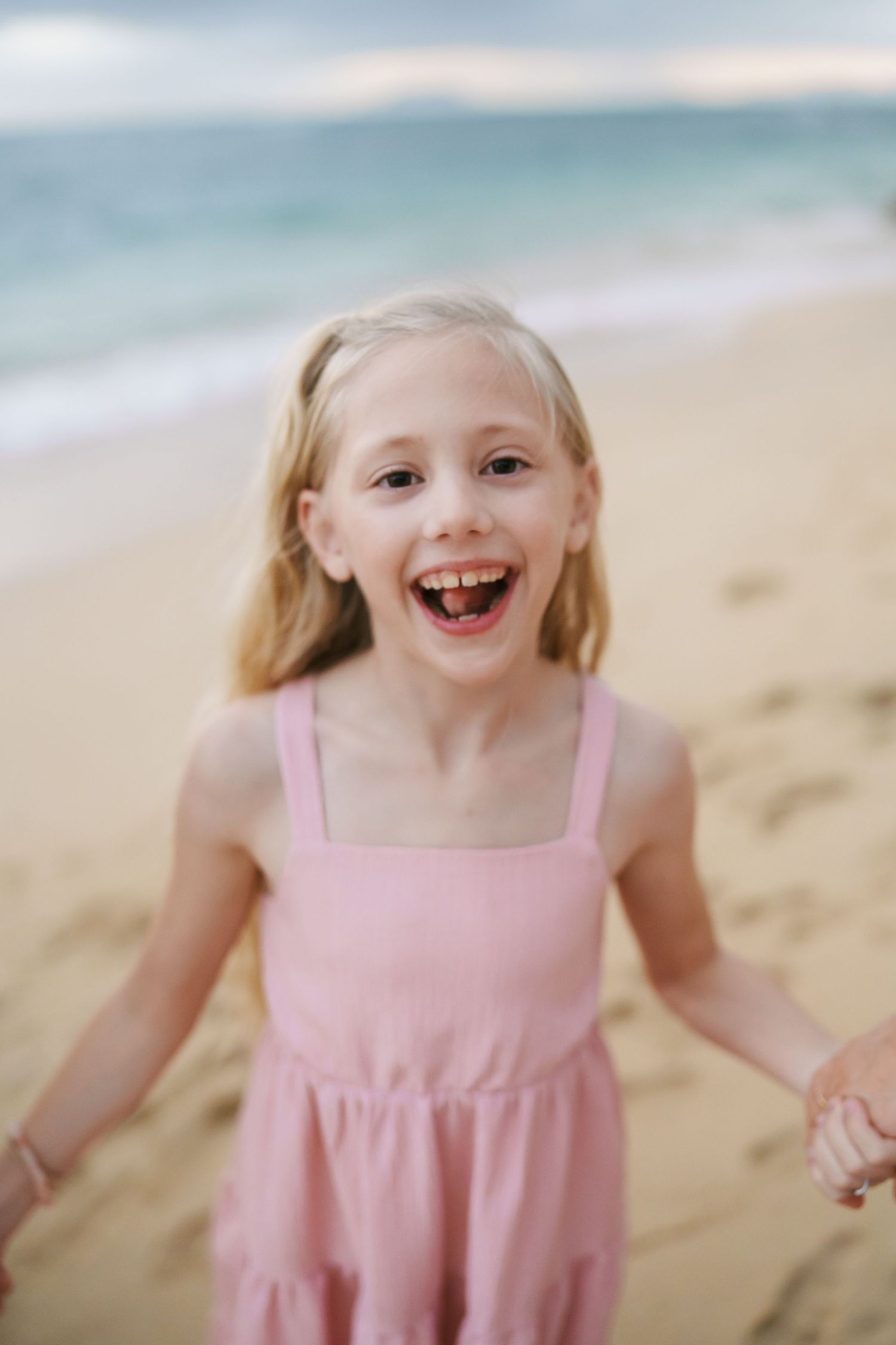 A close-up portrait of a girl laughing and looking directly into the camera at Ka’a’awa Beach, Oahu. A joyful and natural moment with white