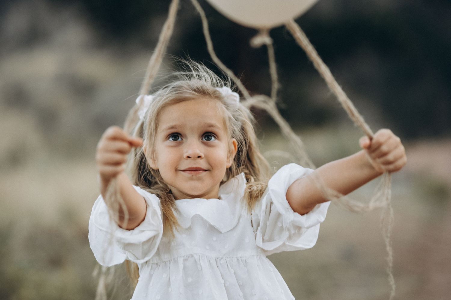 Smiling little girl in white dress holding balloons during a Boulder family photo session at NCAR, Colorado