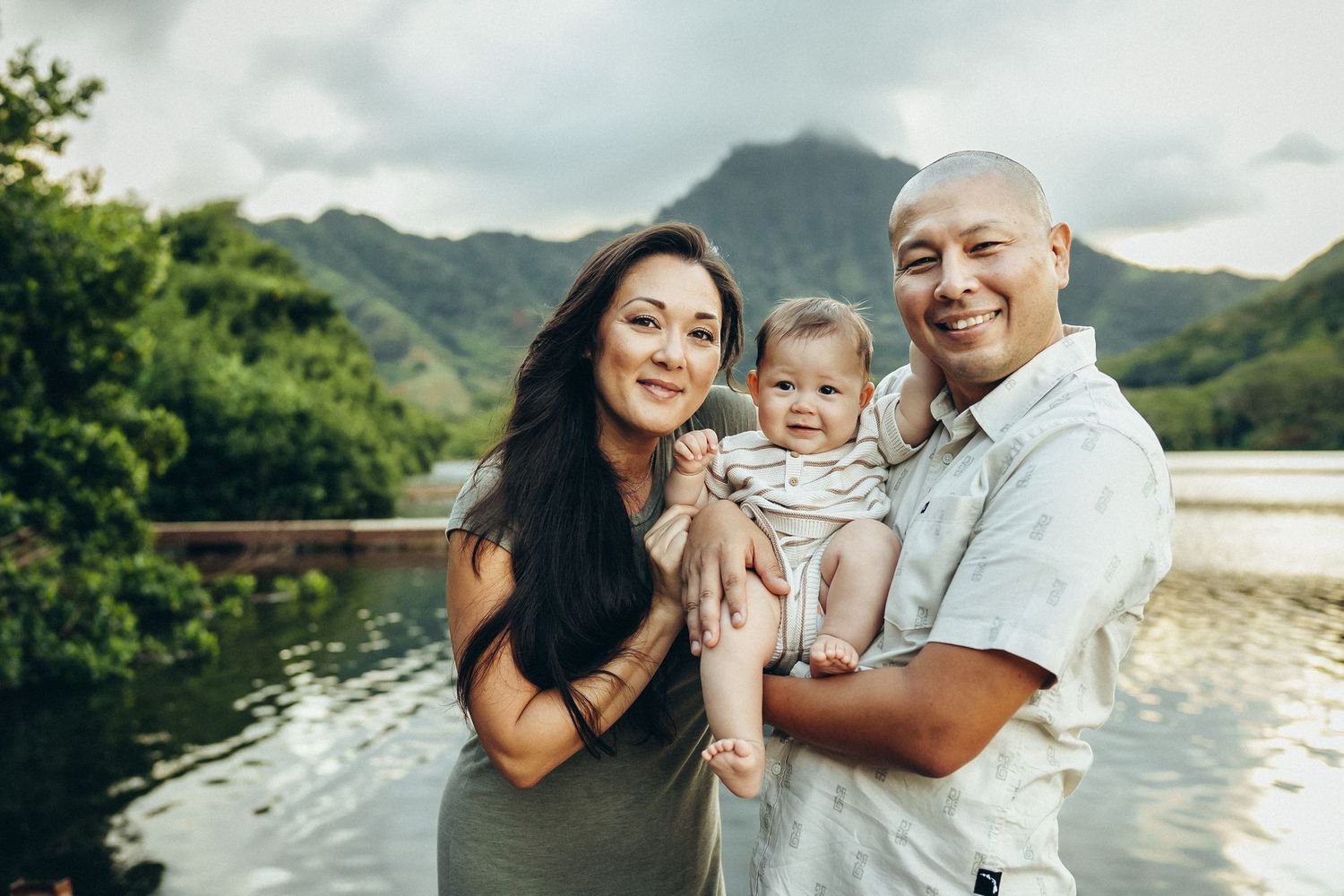 A family shares joyful moments together against a backdrop of lush Hawaiian mountains and scenic waterfront views at Secret Island