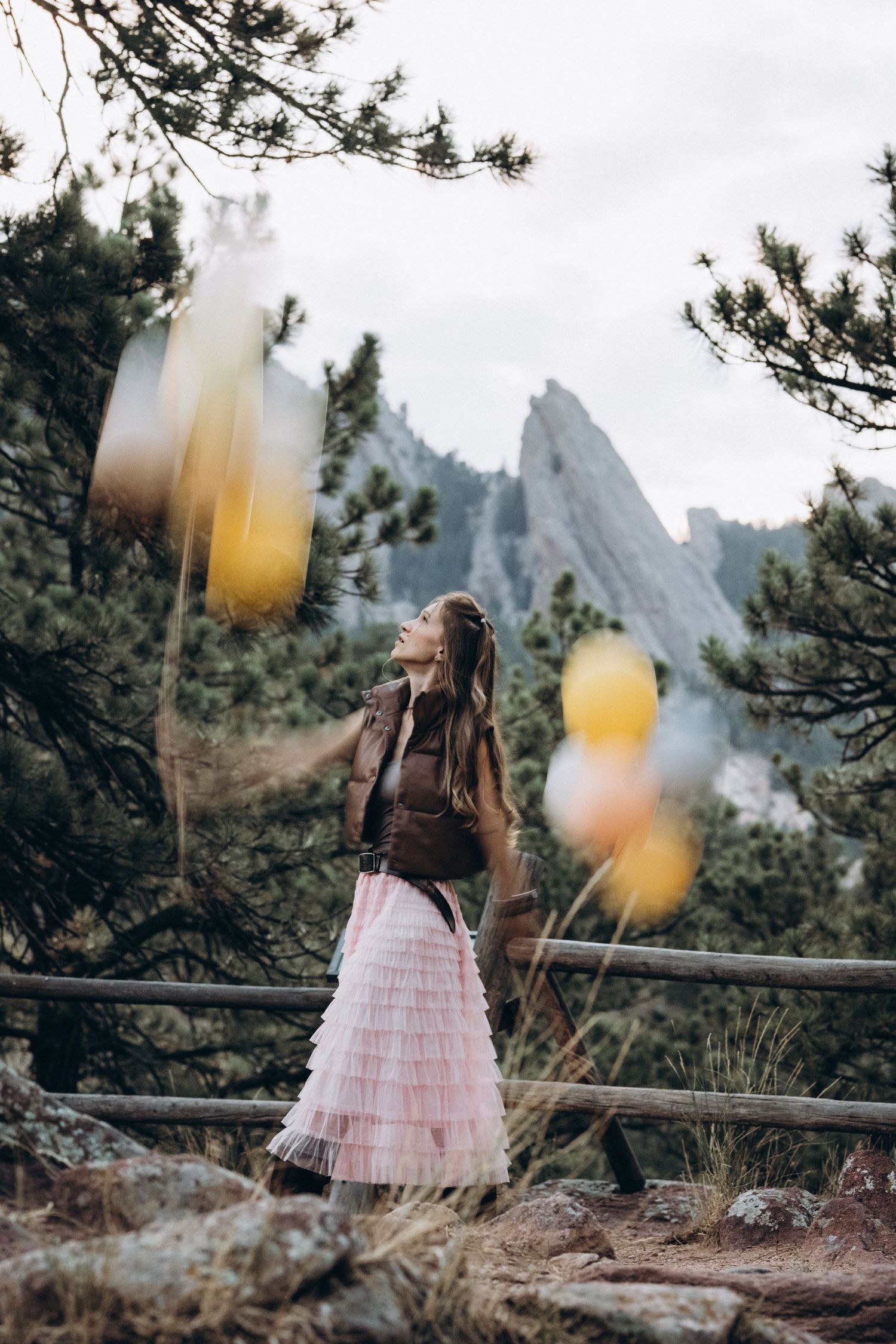 Woman with balloons by a wooden fence and pine trees, Flatirons view, Boulder photographer at NCAR, Colorado