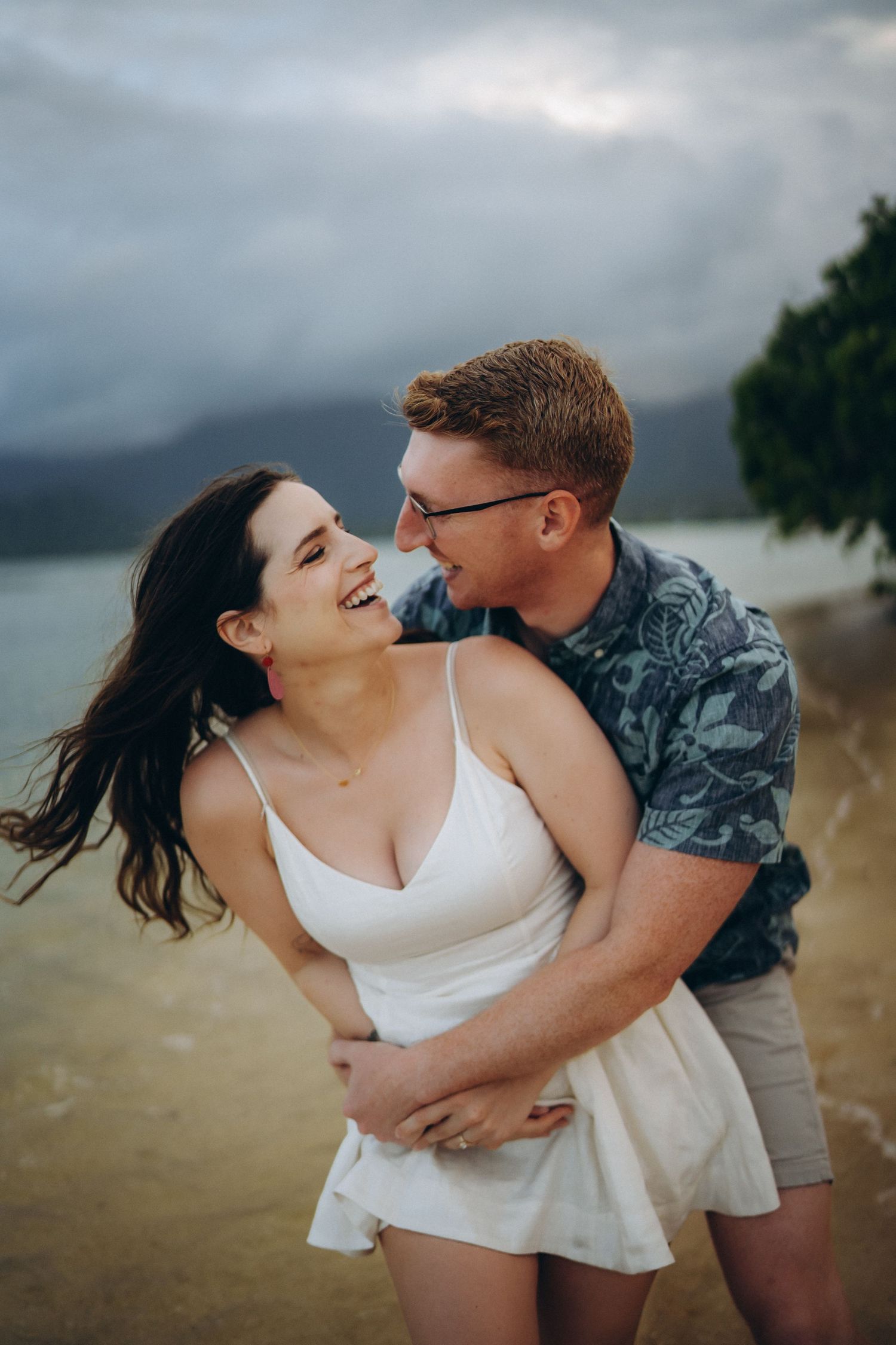 Laughing couple in a close embrace by the water, Kualoa Ranch couples photo session, Oahu photographer, Hawaii