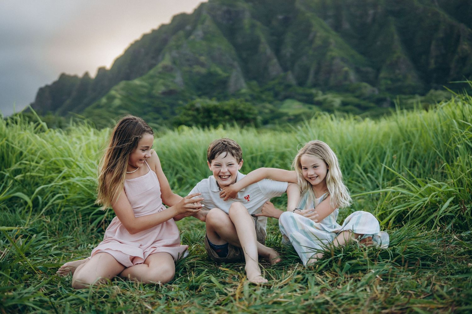 Three children laughing together in tall green grass, Kualoa Ranch family photo session, Oahu photographer, Hawaii