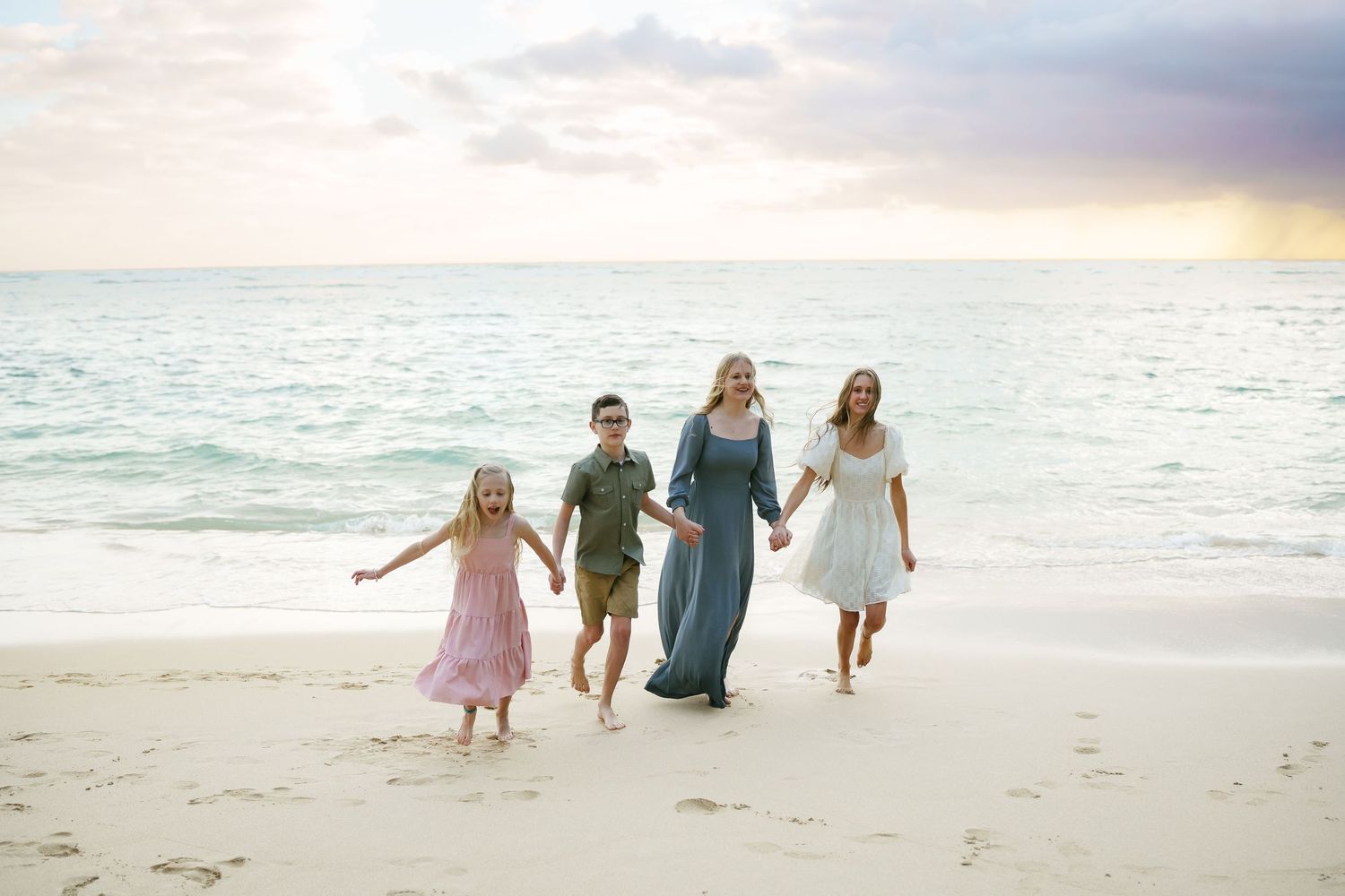 Four children walking hand-in-hand at sunrise on Ka’a’awa Beach Oahu. Waves crashing behind as the siblings enjoy a family session in Hawaii