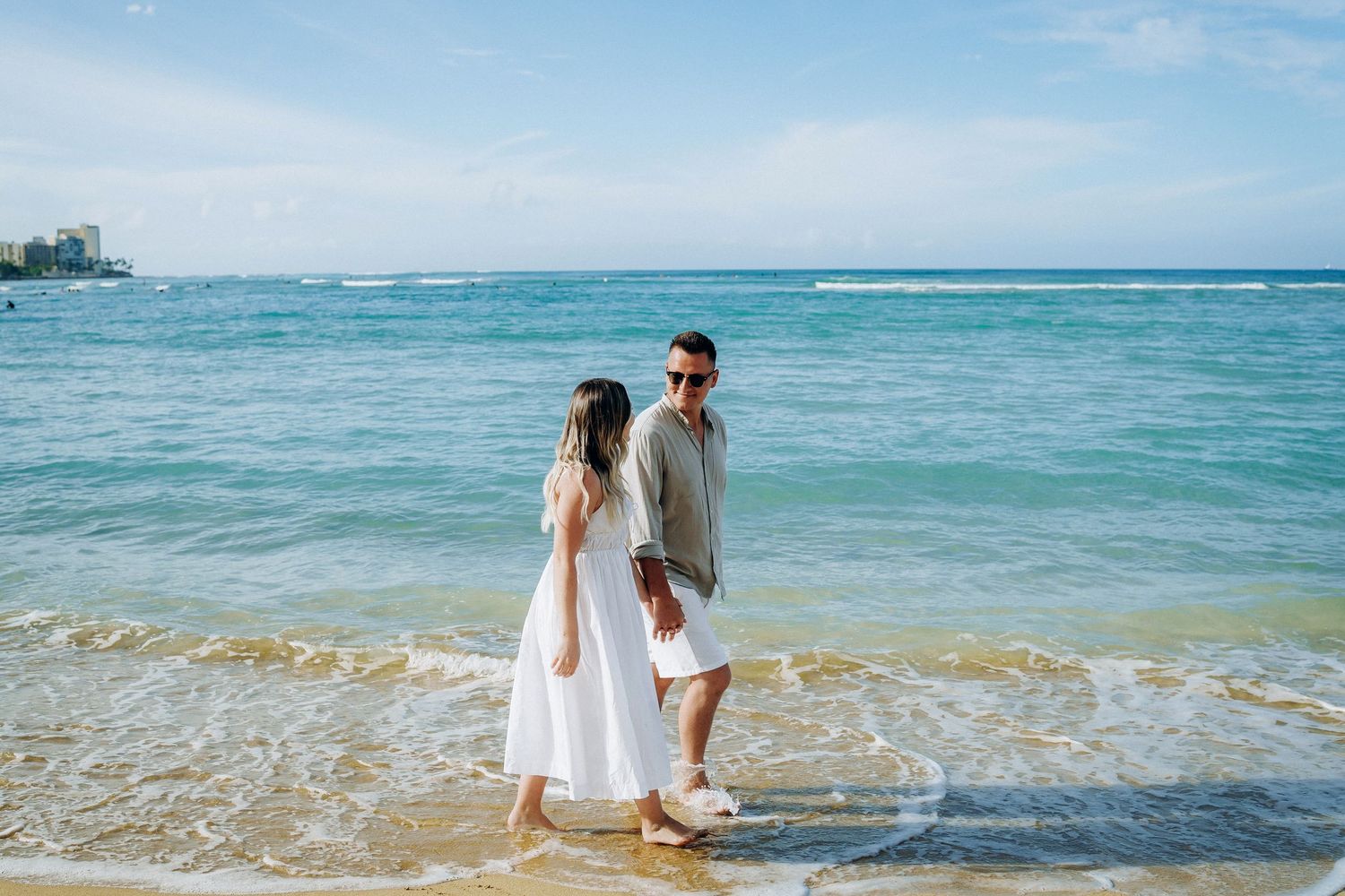 Waikiki mini session. Photographer Oahu Waikiki. A couple walking along the shoreline with a bright turquoise ocean stretching behind them.