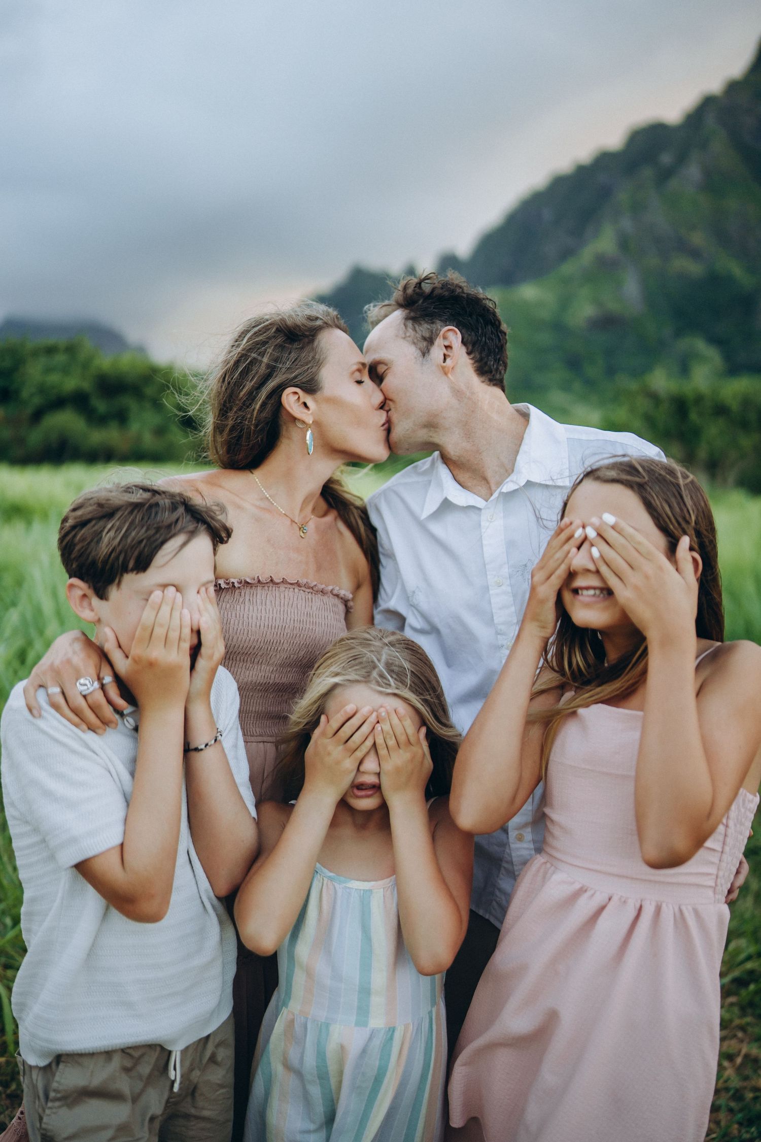 Parents kissing while kids playfully cover their eyes, Kualoa Ranch Oahu family photographer, Hawaii