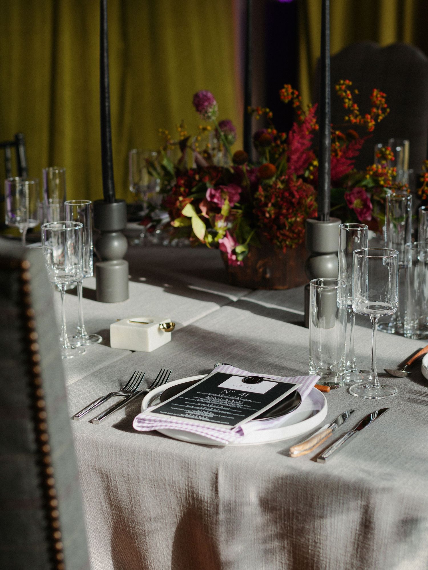 Elegant table settings at a formal dinner with white linens, glassware, and colorful floral arrangements in the background.