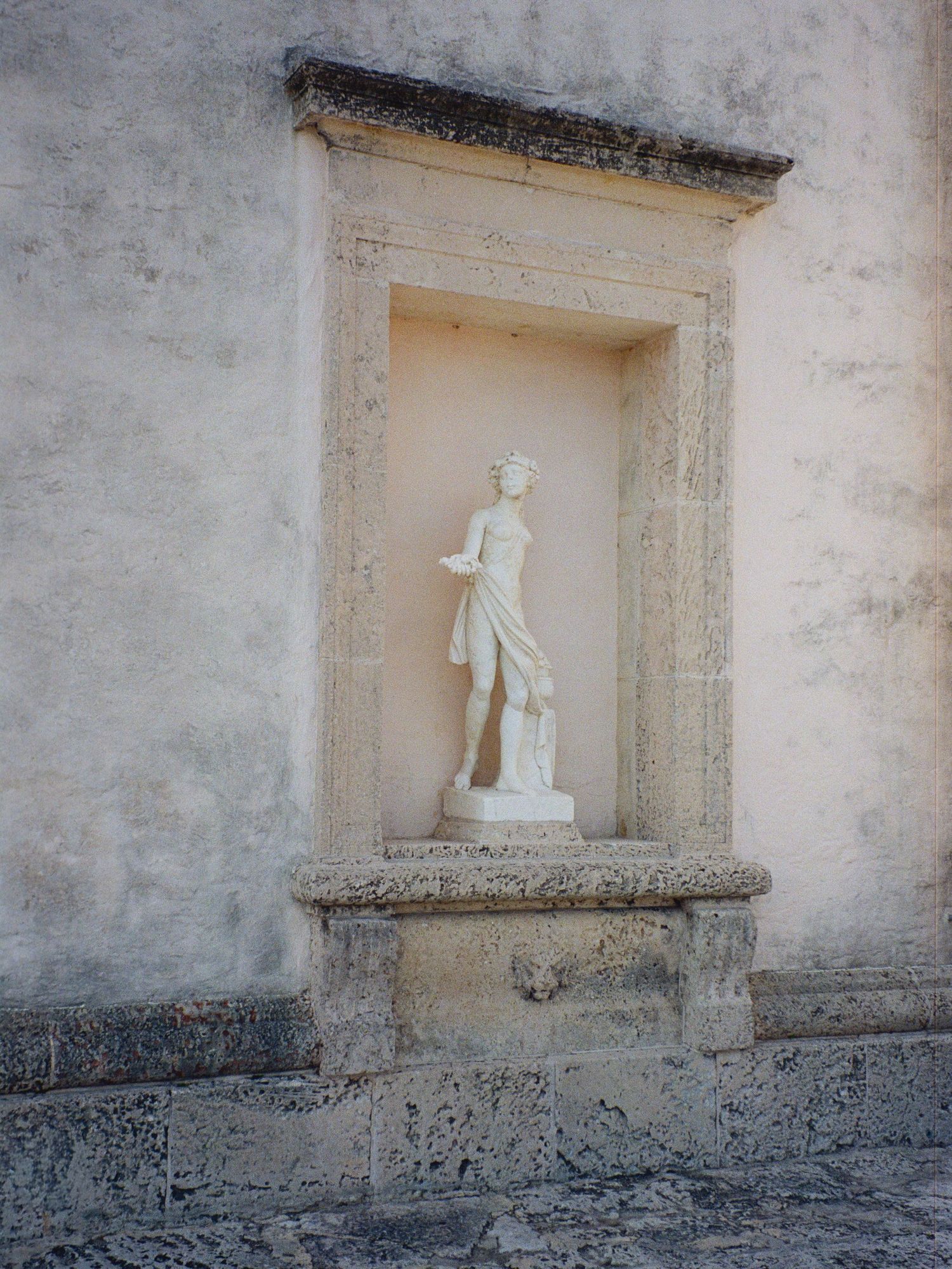 White classical statues displayed in wall alcoves of a weathered stone building exterior.