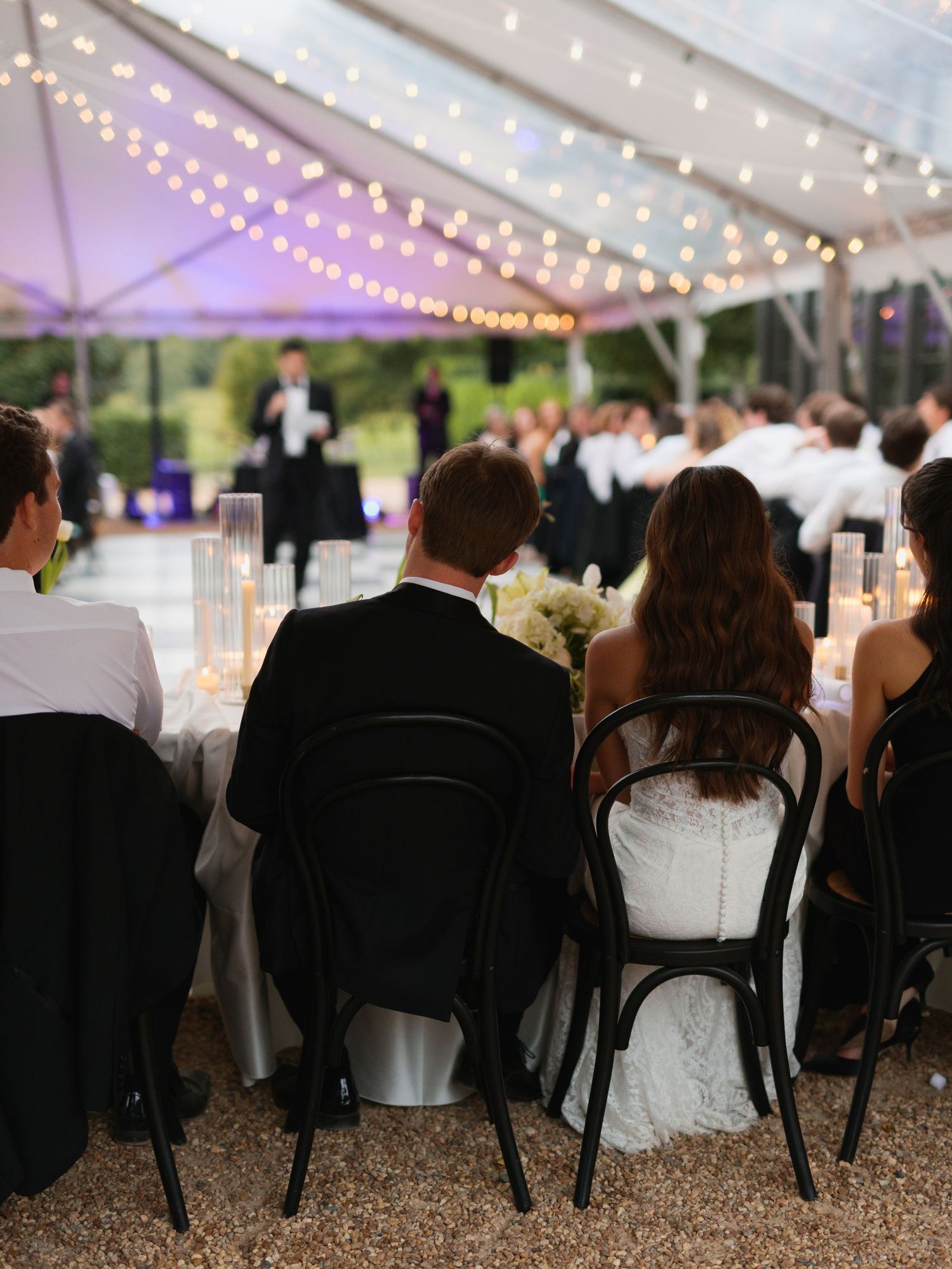 Wedding guests seated under a white tent with twinkling string lights creating a romantic evening atmosphere.