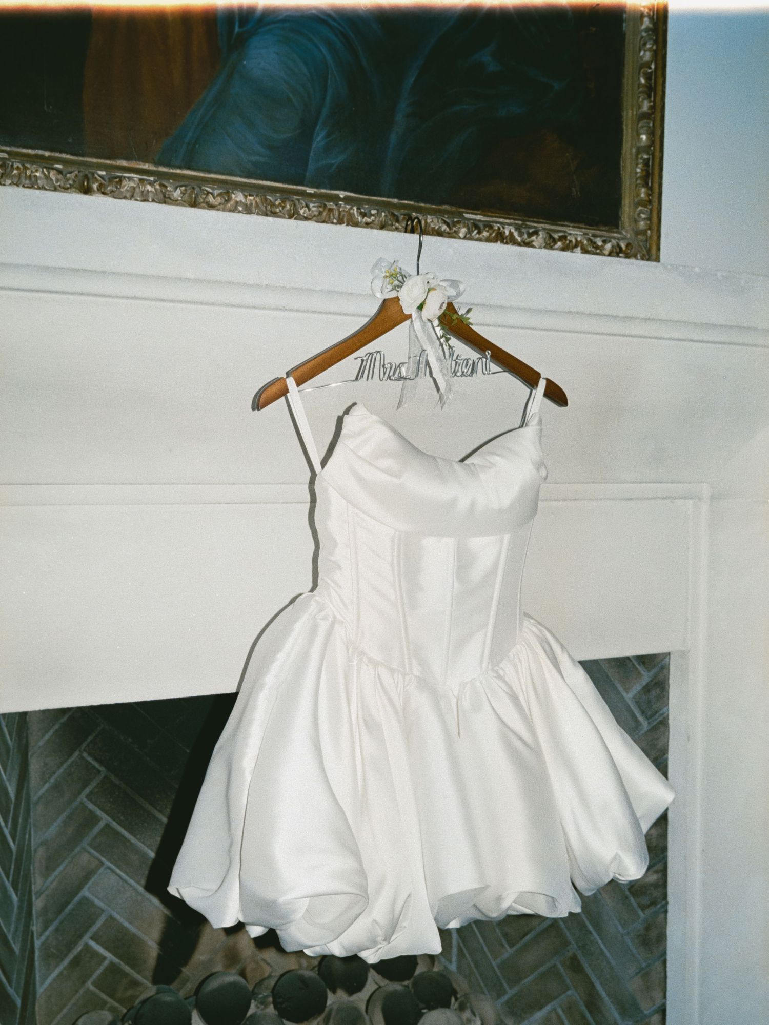A series of white baby dresses or garments hanging on wooden hangers displayed against a light colored wall.