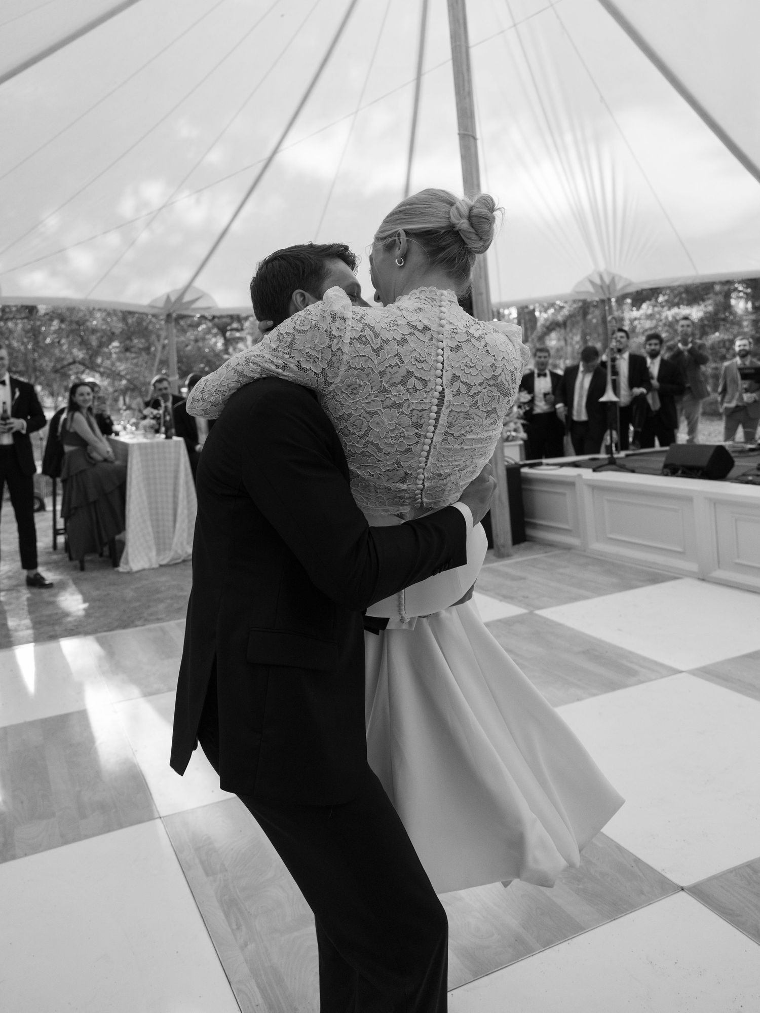 Bride and groom share first dance in black and white photo under elegant wedding tent.