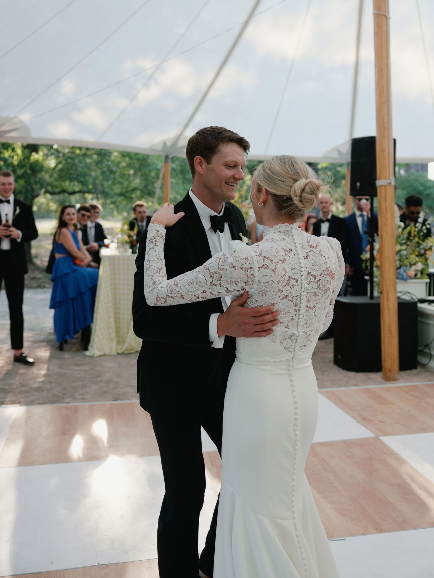 Bride and groom share their first dance under a white tent at an outdoor wedding reception.
