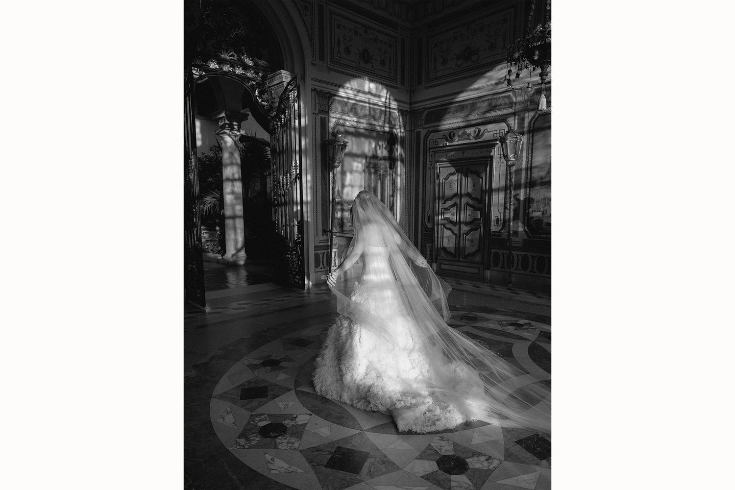 A bride in a flowing white gown and veil stands in an ornate cathedral with arched hallways and intricate architecture.