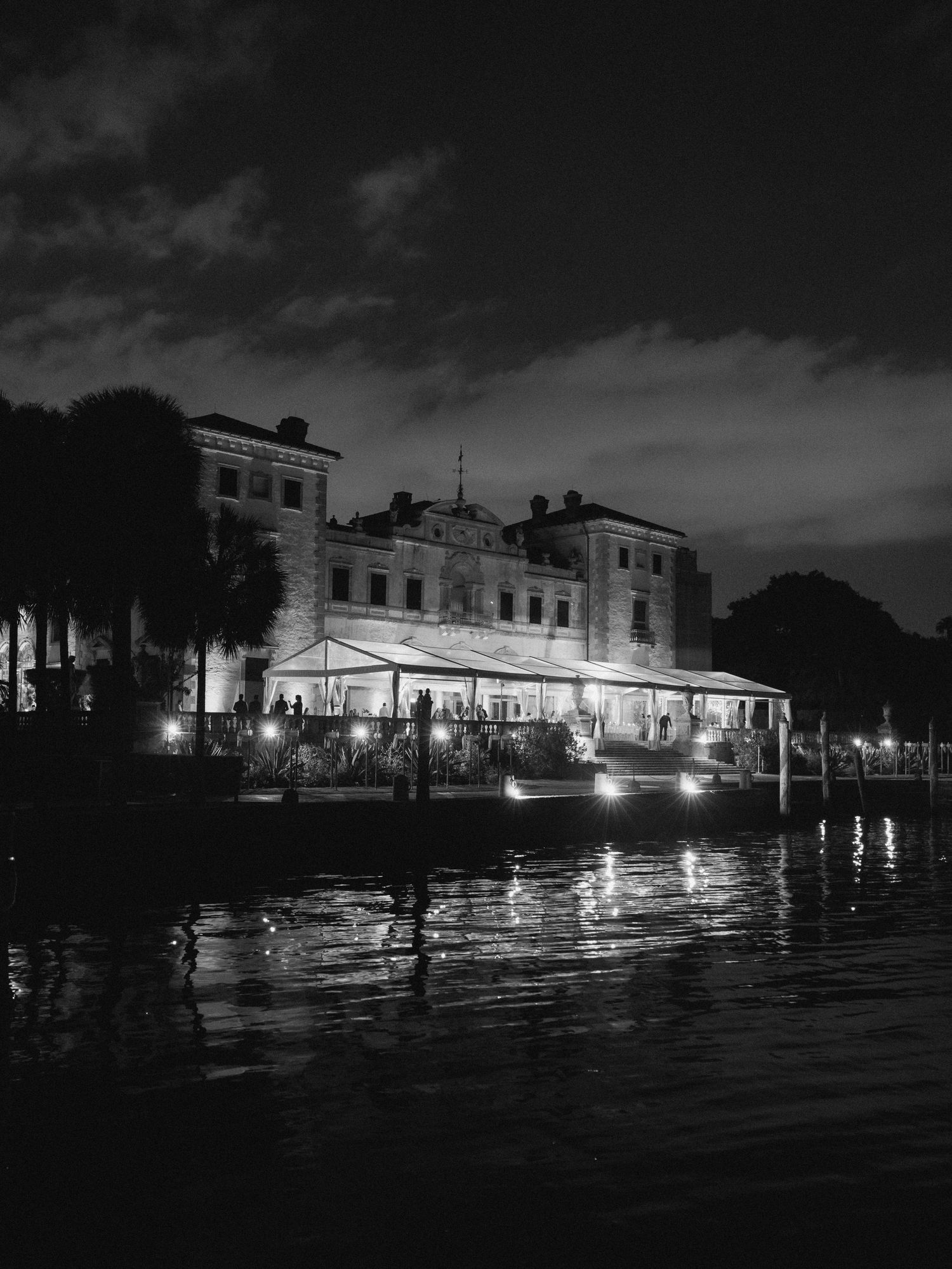 Dramatic black and white nighttime cityscape showing flooded streets with illuminated buildings reflecting on dark waters.