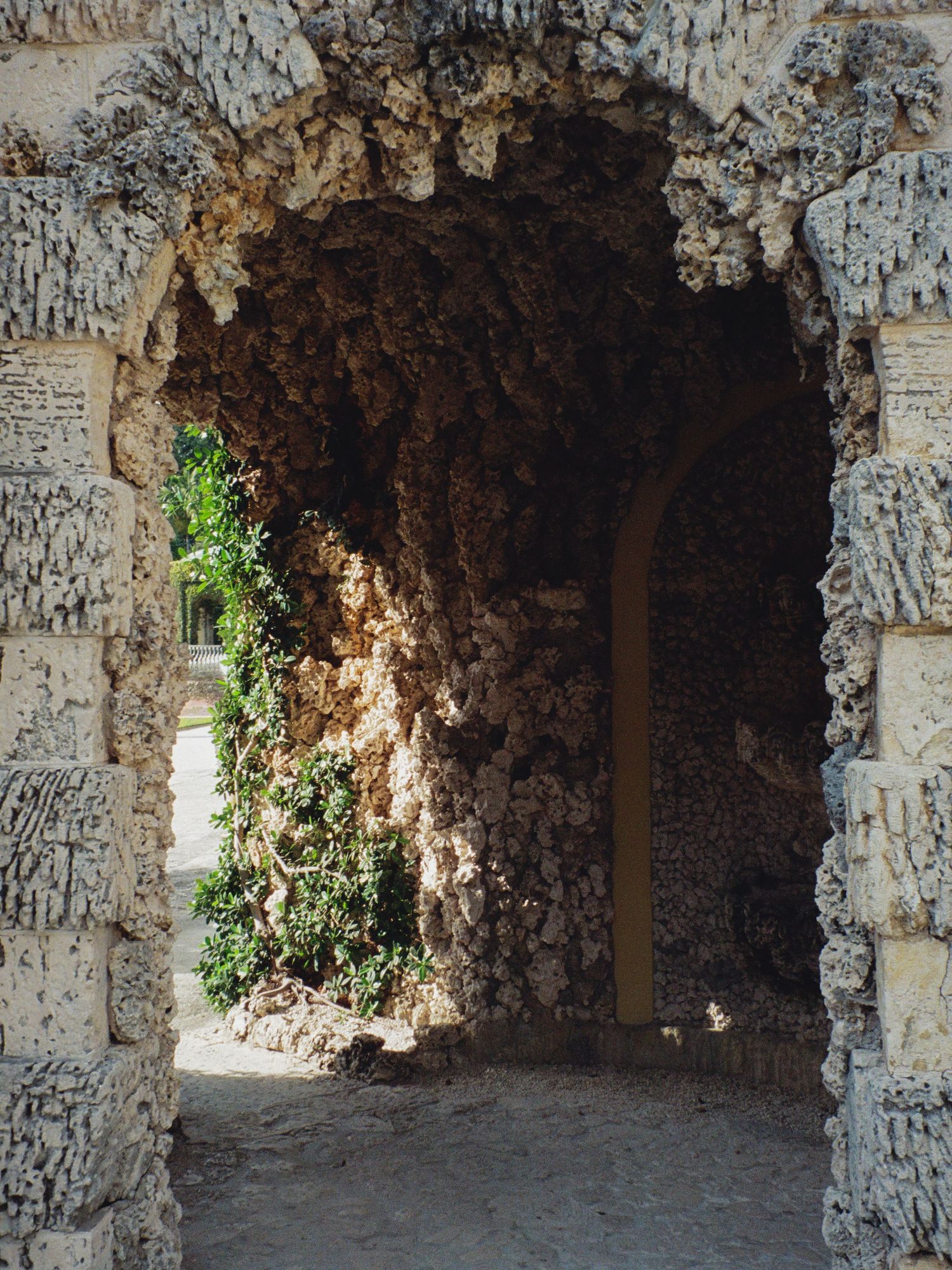 A series of stone archways with graffiti leading into a dark cave-like corridor with glimpses of natural light and foliage.