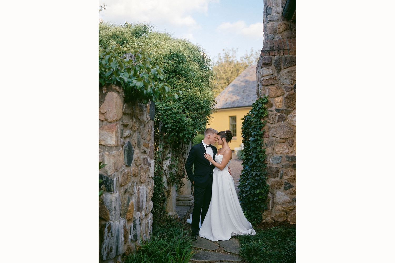 A romantic wedding couple shares a moment in the stone courtyard of a historic venue with lush green ivy growing on walls.