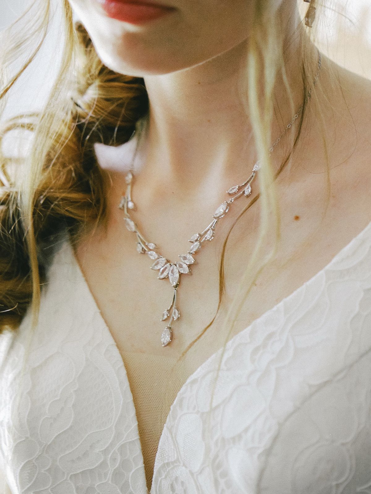 Delicate crystal necklace with floral design worn with white lace wedding dress in soft natural lighting.