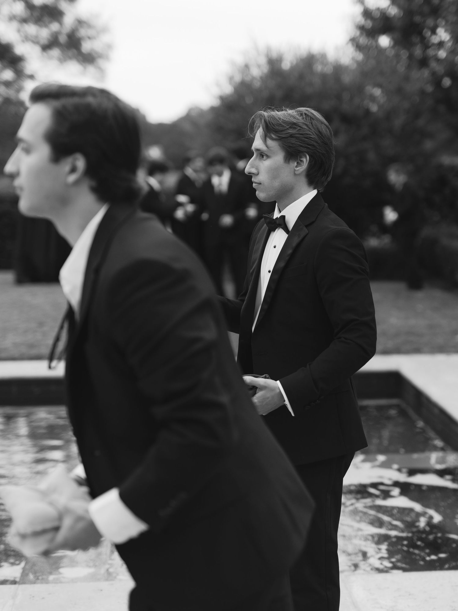 A black and white photo sequence shows a group in formal attire leaning forward in synchronized motion by a pond.