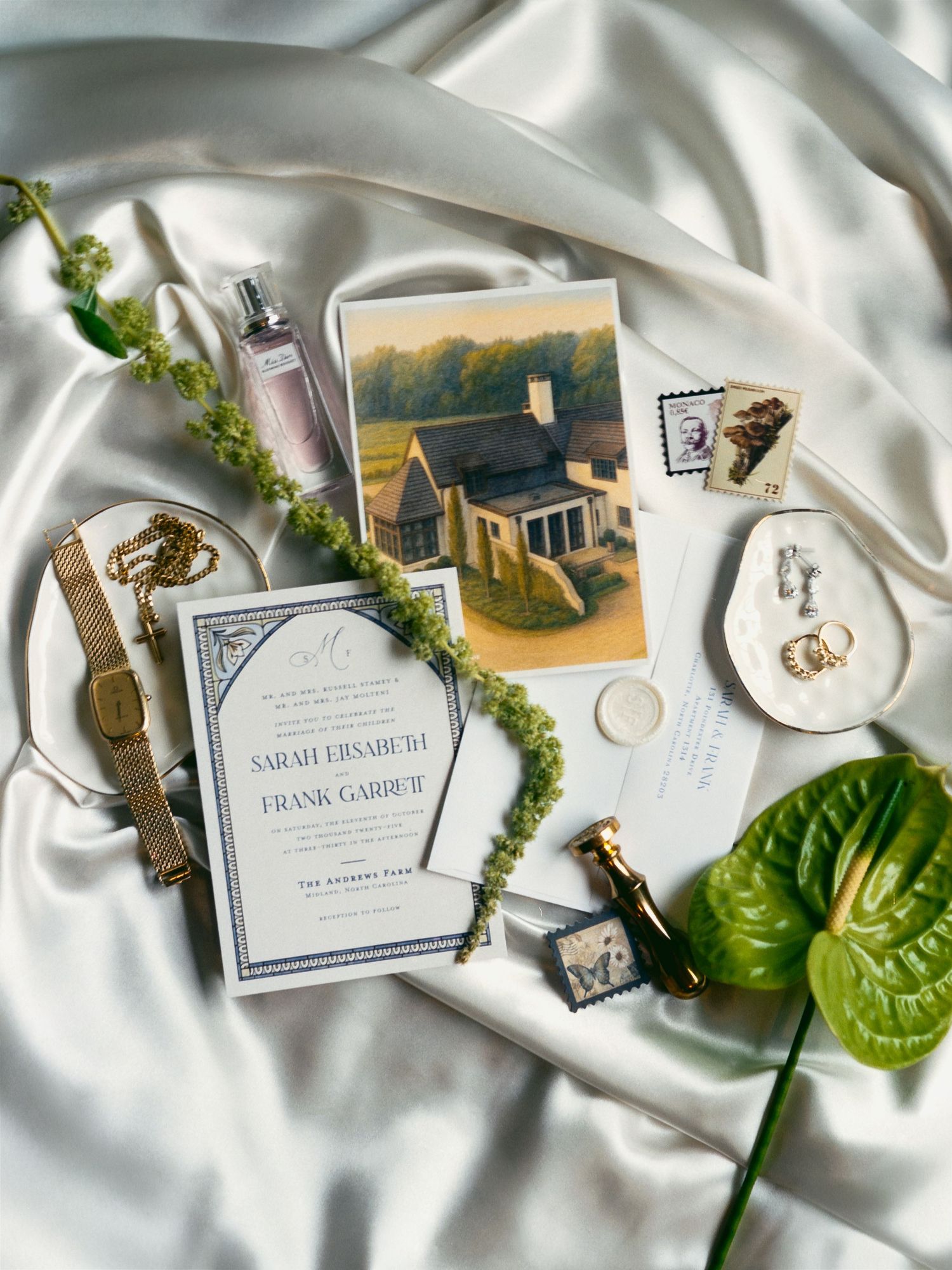 Wedding invitation cards and decorative elements arranged on white silk fabric with greenery accents and elegant details.
