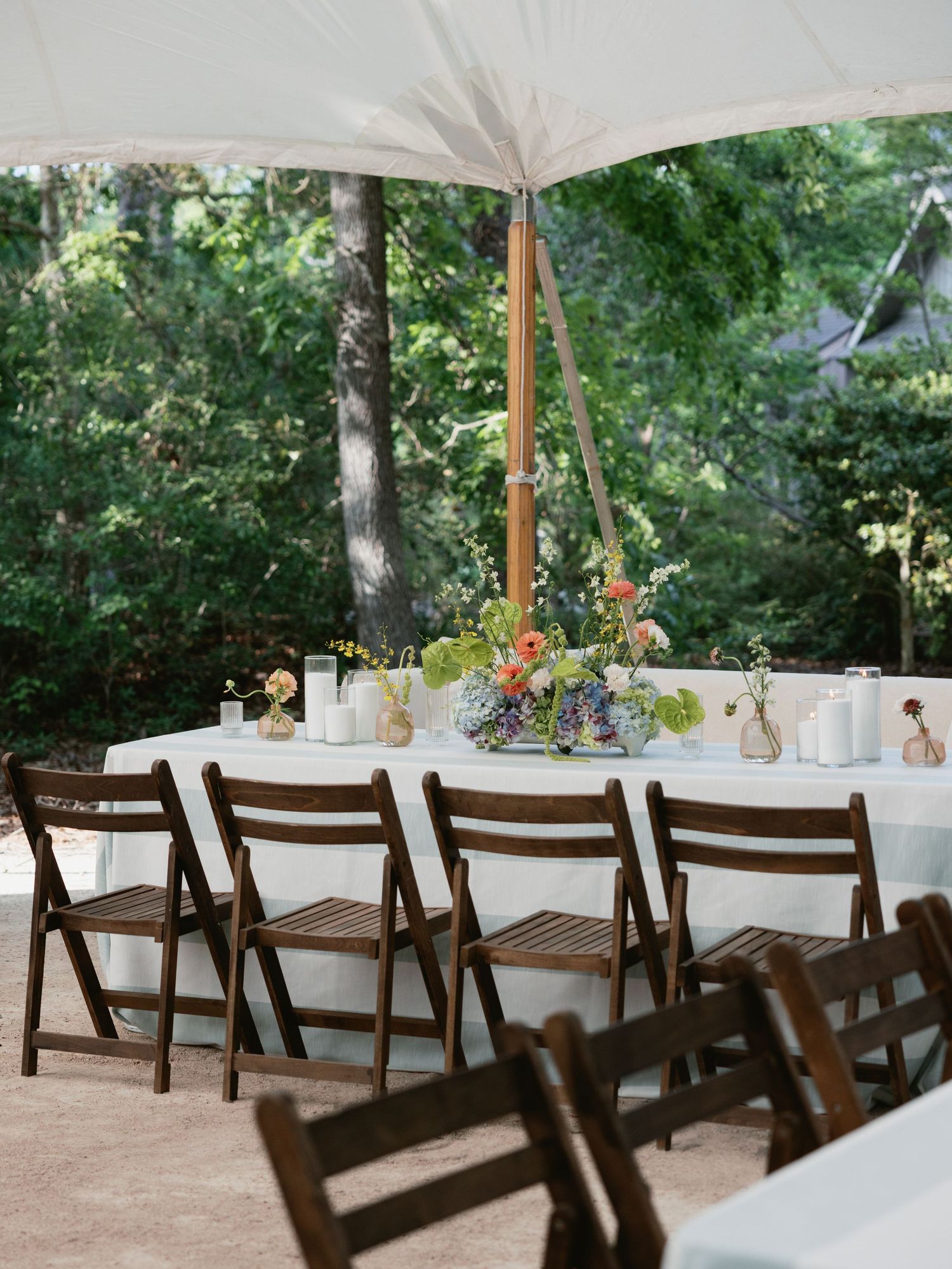 Elegant outdoor wedding reception under white tent with dark wood folding chairs and colorful floral centerpieces.