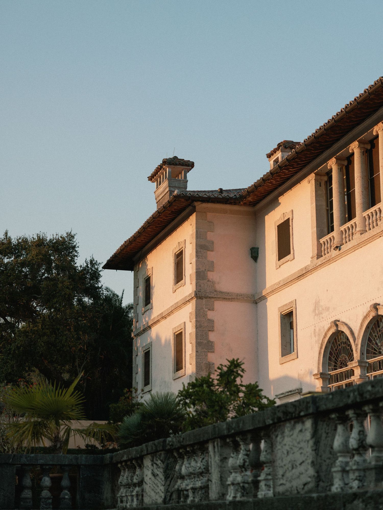 Historic Mediterranean-style villa with white walls and terracotta roof tiles set against lush greenery at dusk.