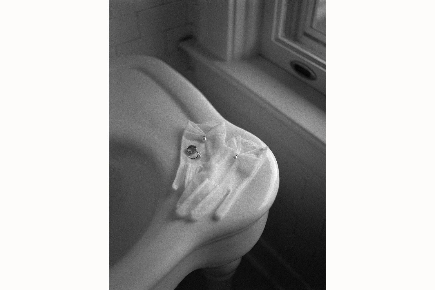 A black and white photograph shows a small kitten curiously peering out from behind a window or glass surface.