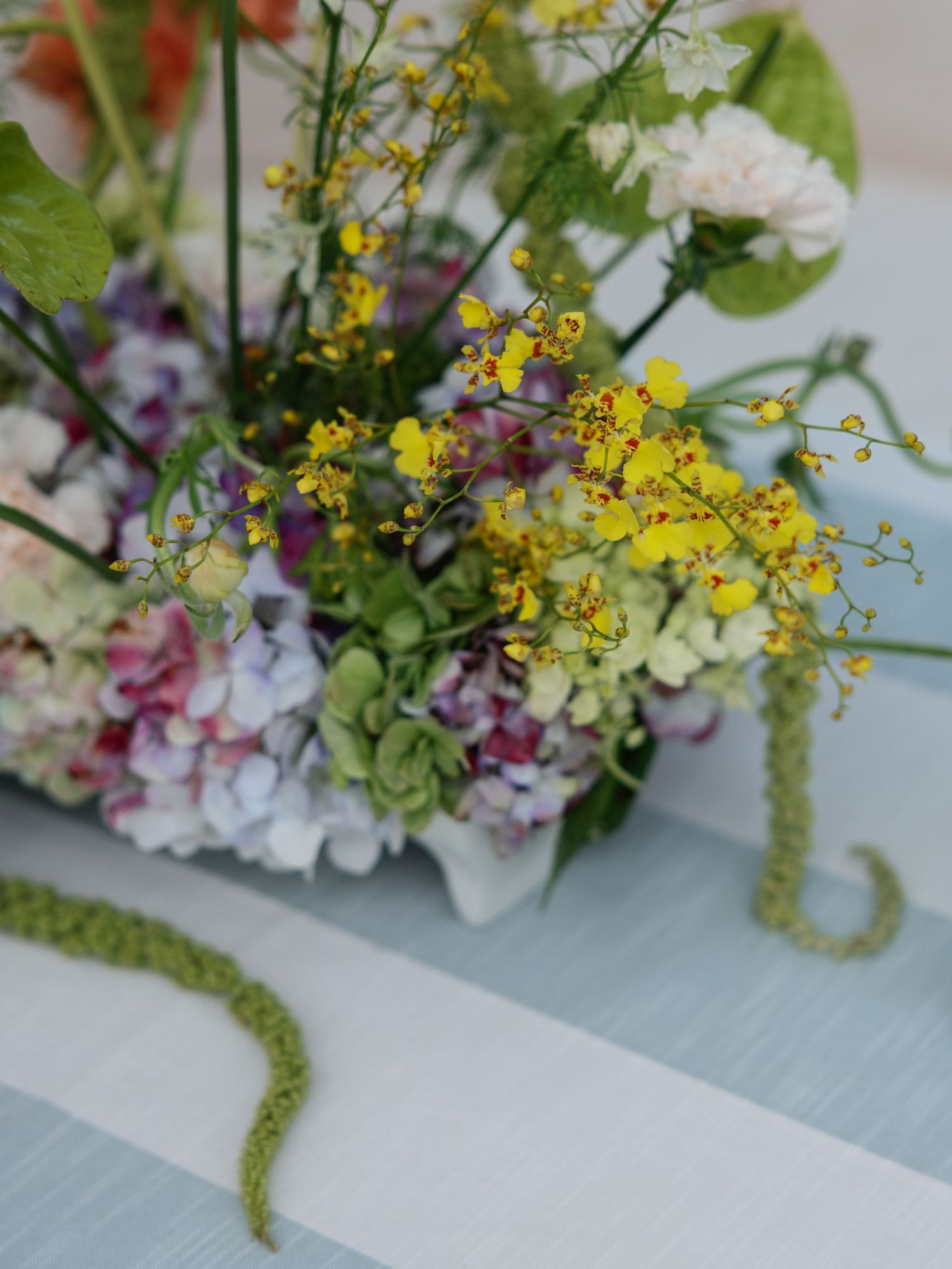 Colorful floral arrangement with yellow, purple, and white blooms on a light blue striped table.