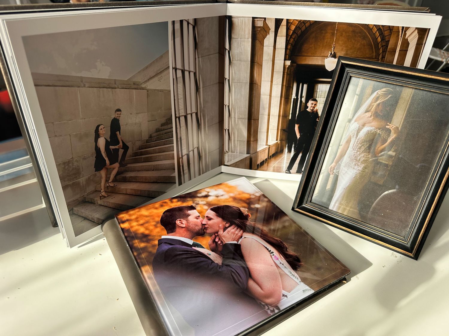Wedding photo albums and framed portraits arranged on white surface.
