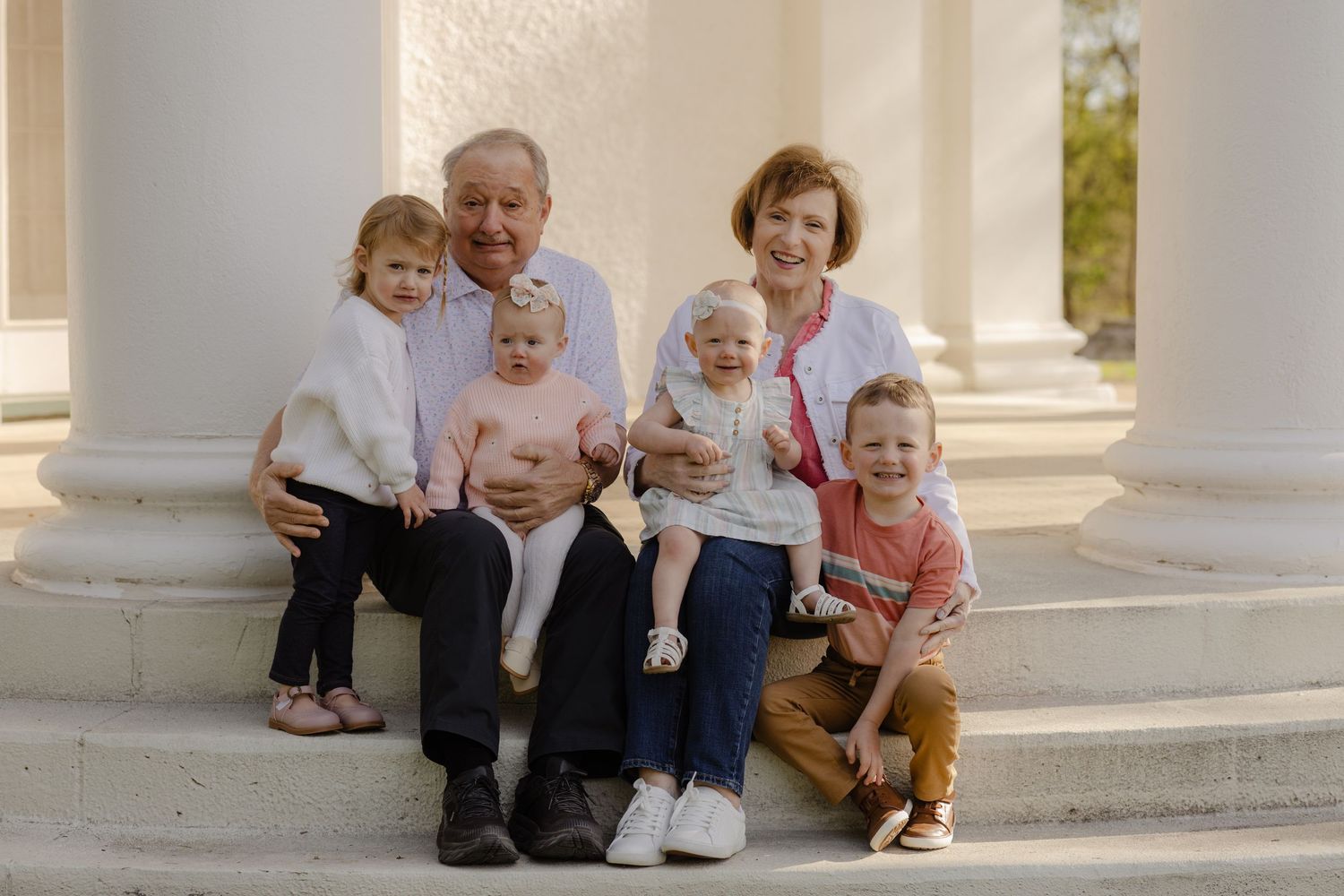 A multigenerational family portrait on white stone steps outdoors.