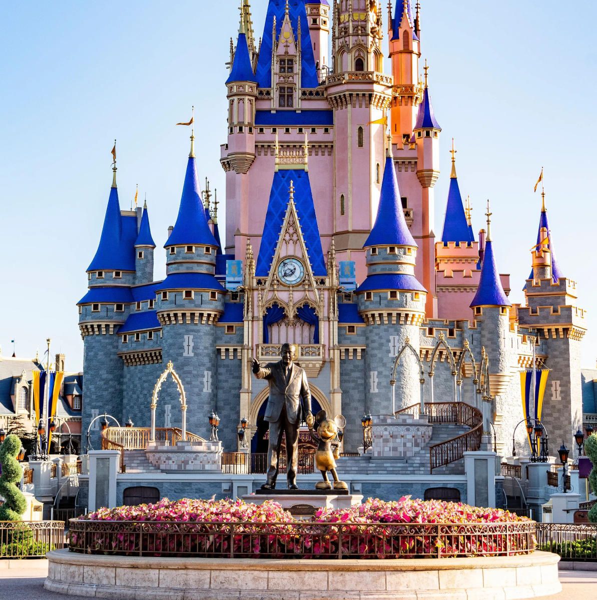 Golden Walt Disney and Mickey Mouse statue in front of Cinderella Castle with blue spires at Magic Kingdom, Walt Disney World.
