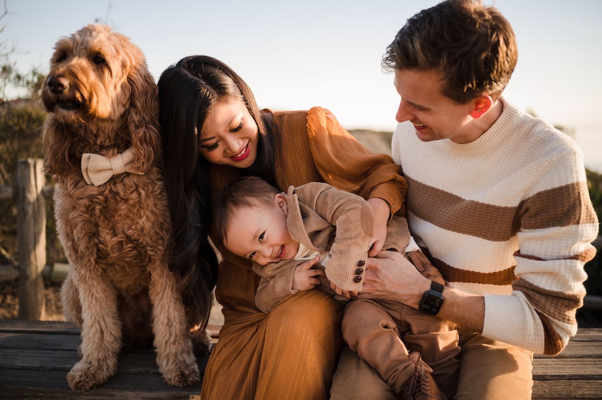 Happy young family with a fluffy goldendoodle dog smiling together outdoors in warm autumn tones.