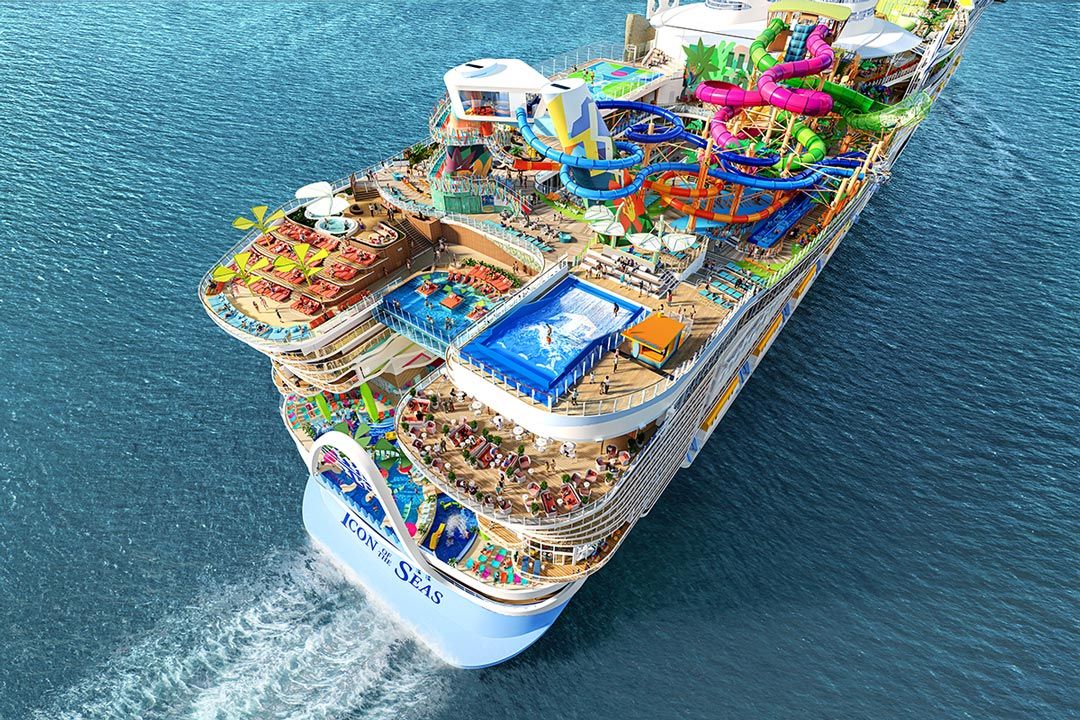 Aerial view of a massive Royal Caribbean cruise ship featuring colorful water slides, pools, and packed decks sailing on blue ocean waters.