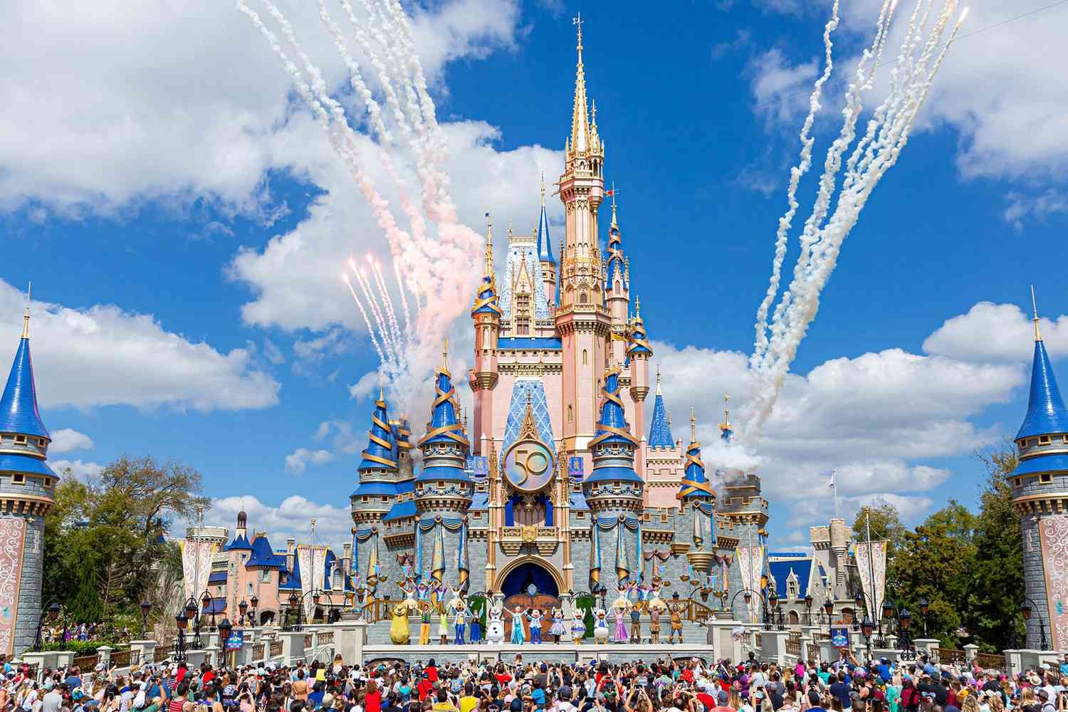 Cinderella Castle at Walt Disney World Magic Kingdom with colorful fireworks display and crowds of visitors on a sunny day.