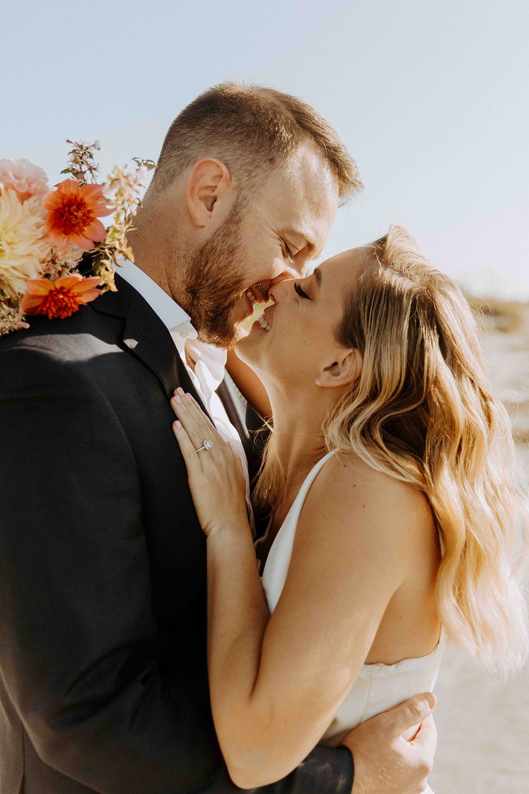Bride and groom sharing a romantic almost-kiss moment with vibrant orange and pink wedding bouquet outdoors.