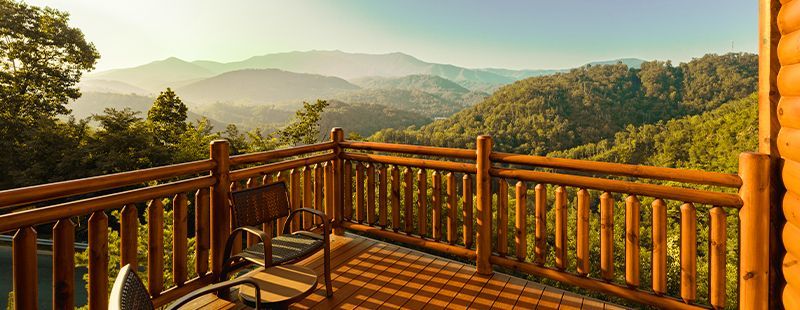 Rustic log cabin deck with rocking chair overlooking stunning smoky mountain forest valley at golden sunset.