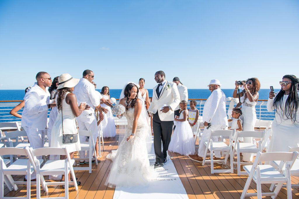 Elegant outdoor wedding ceremony on a cruise ship deck with guests in white attire and ocean backdrop.