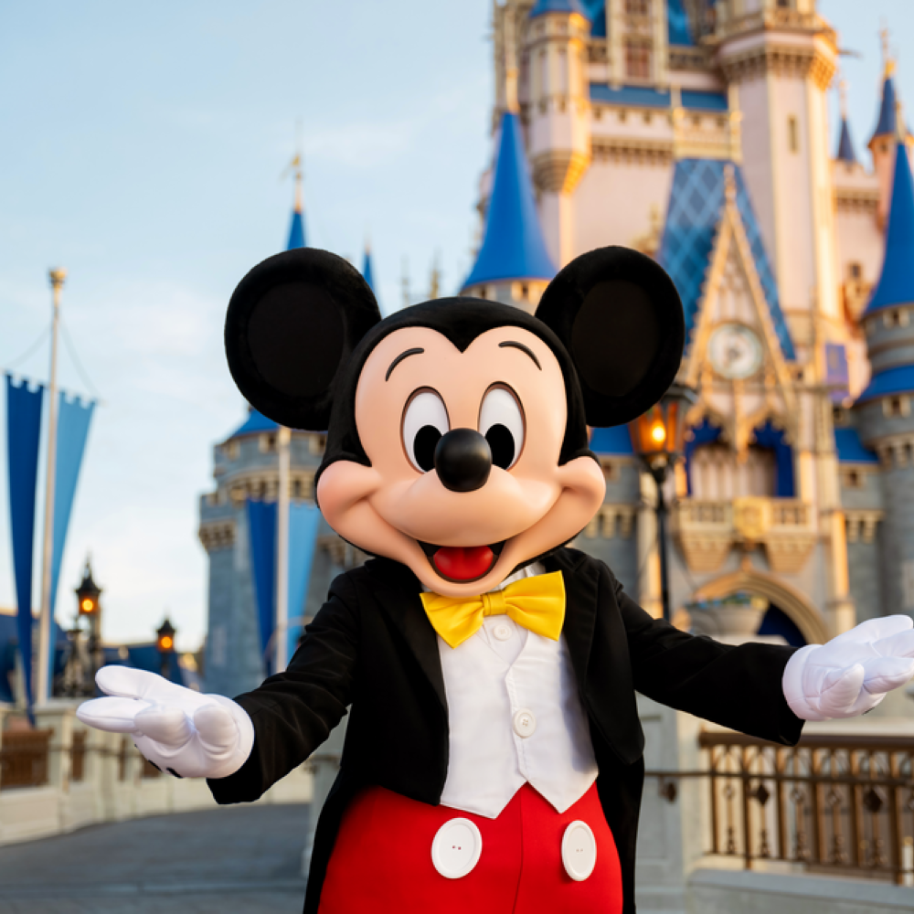 Mickey Mouse character in tuxedo poses in front of Cinderella Castle at Walt Disney World Magic Kingdom.