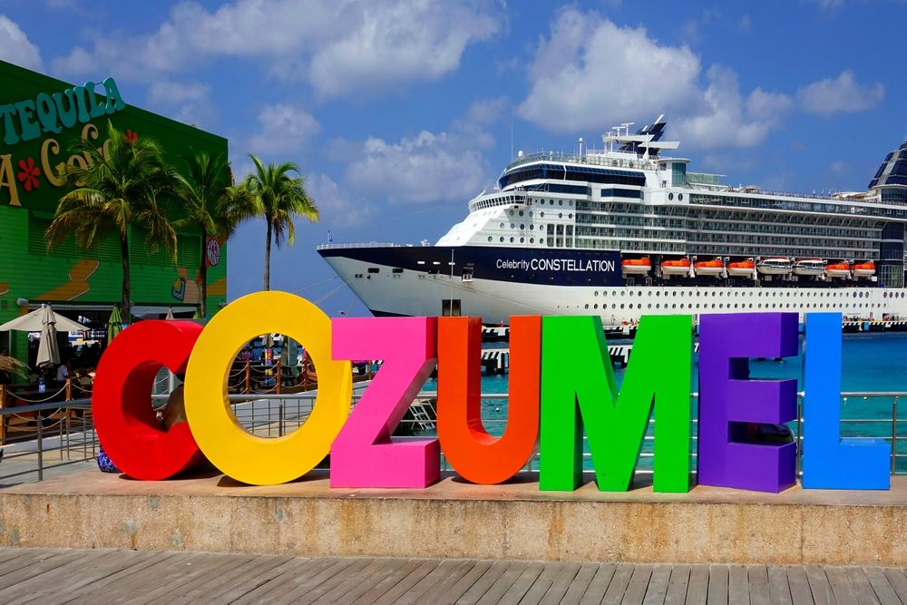 Colorful COZUMEL sign on waterfront with Celebrity Constellation cruise ship docked in background, Mexico.