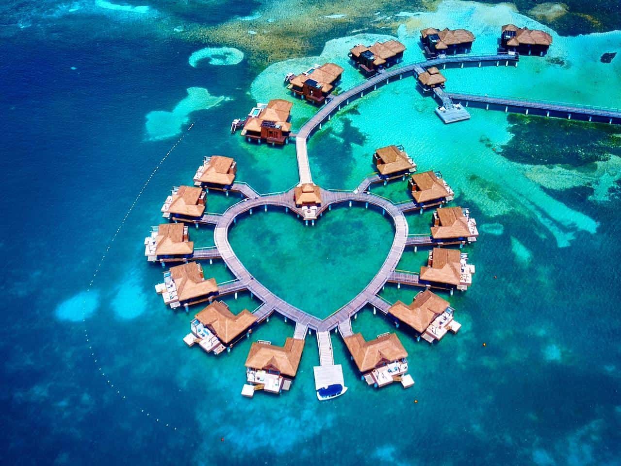 Aerial view of heart-shaped overwater bungalows resort surrounded by turquoise blue ocean waters in the Maldives.