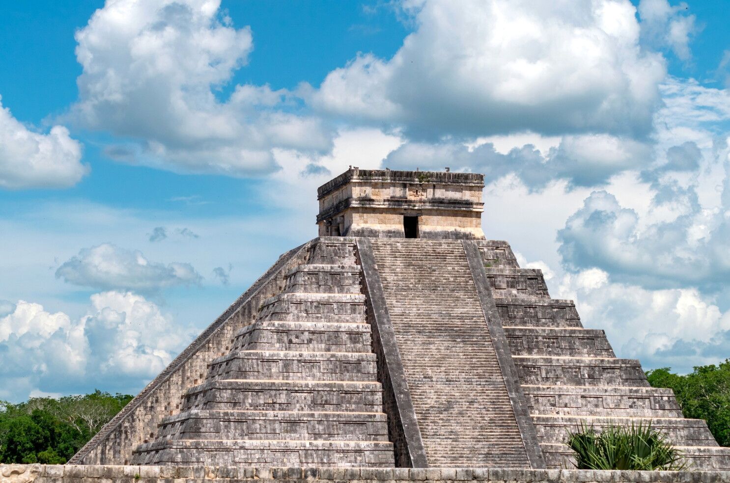 El Castillo pyramid at Chichen Itza, Mexico, under a bright blue sky with white clouds.