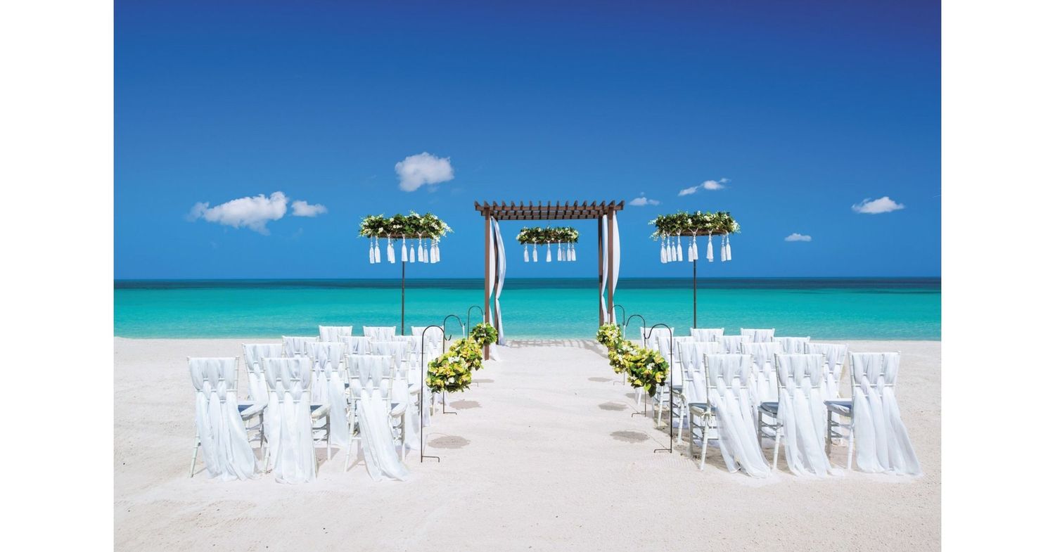 Elegant beach wedding setup with white chairs, floral arch, and turquoise ocean backdrop on a pristine sandy shore.
