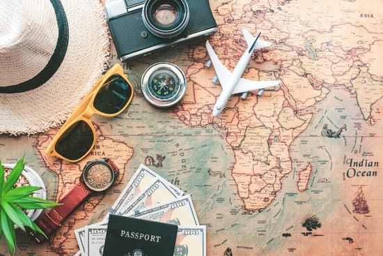 Travel flat lay with passport, money, sunglasses, camera, compass, toy plane, and hat on a world map.