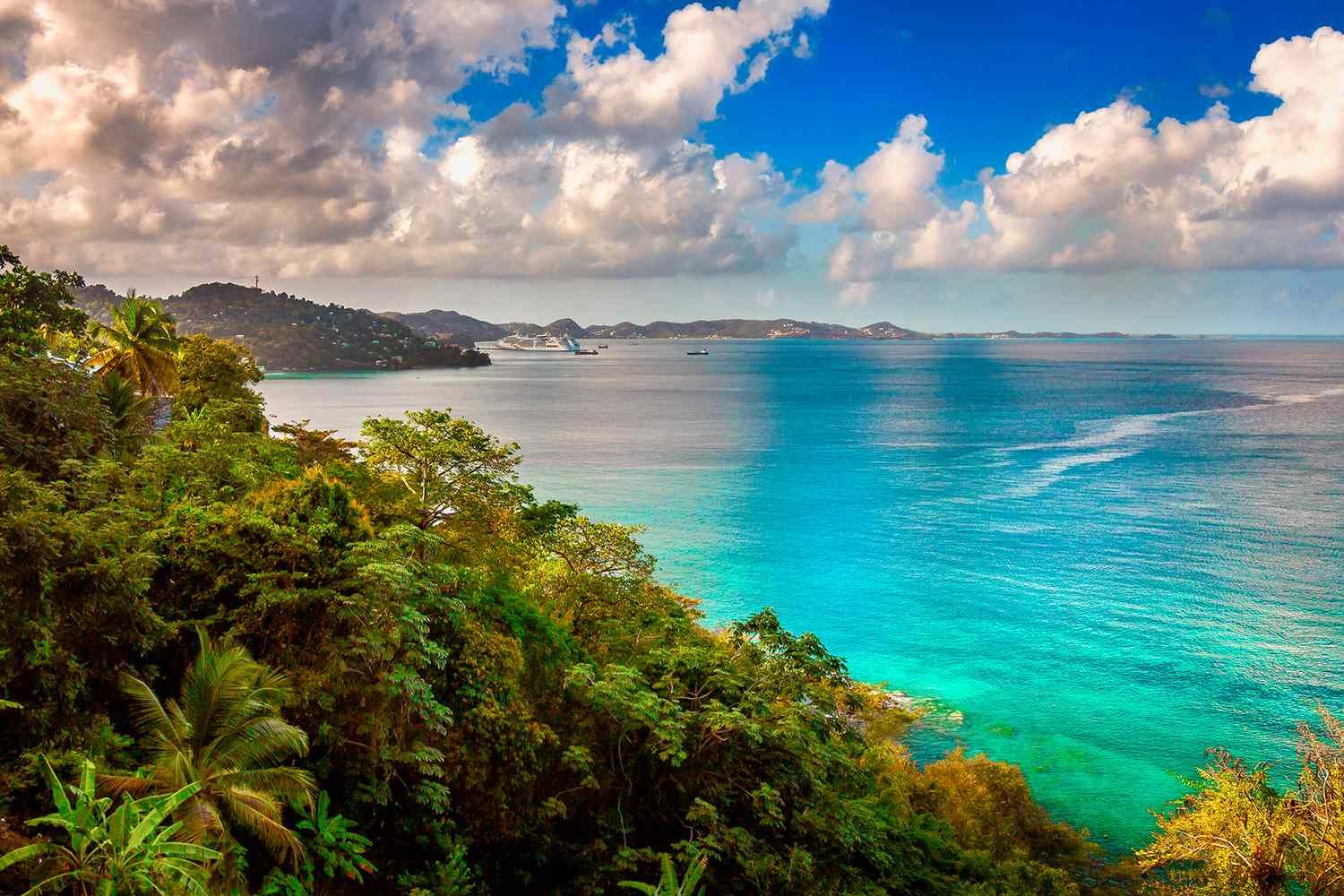 Aerial view of a tropical island coastline with lush green jungle, turquoise ocean waters, and dramatic cloudy sky.