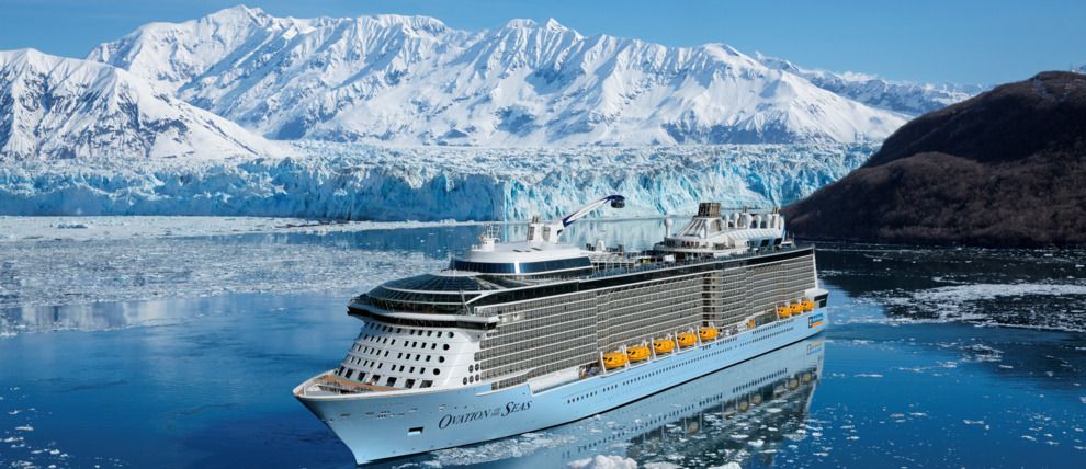 Royal Caribbean cruise ship sailing in Alaska with stunning glaciers and snow-capped mountains reflected in calm waters.