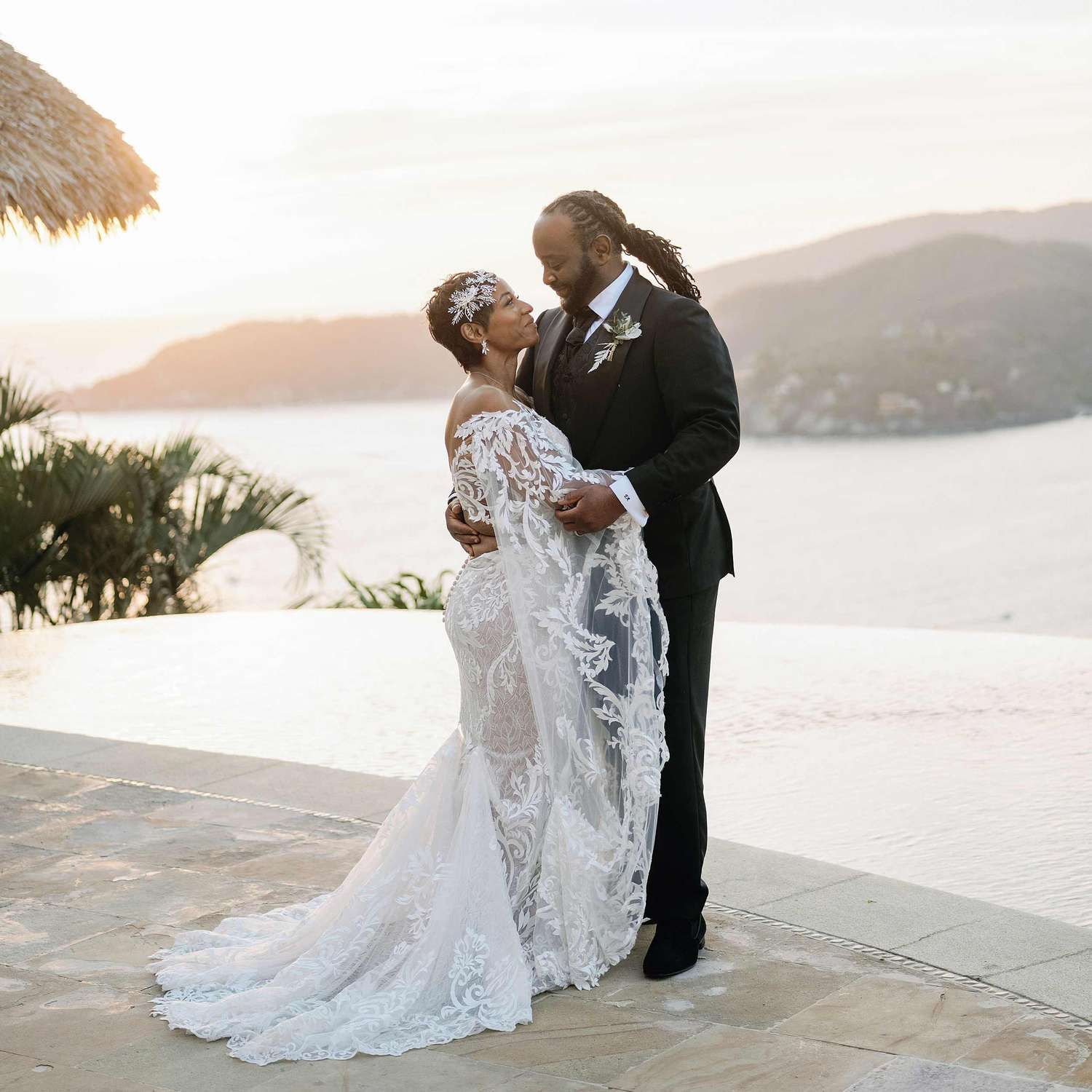 Couple sharing a romantic moment in wedding attire at a tropical oceanview venue during golden hour sunset.