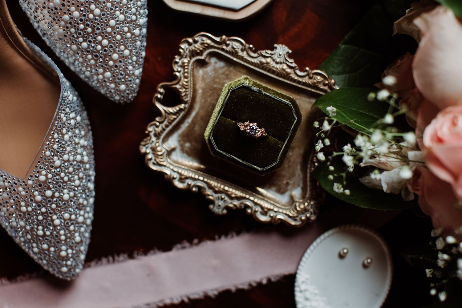 Elegant wedding details including rings, perfume bottles, and delicate floral arrangements on dark background.