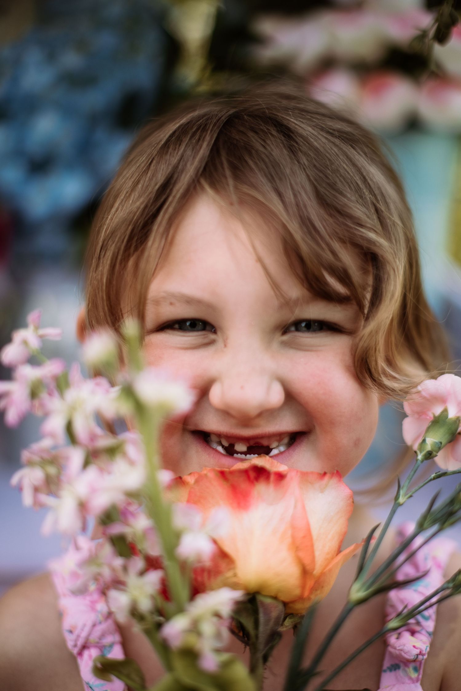 Child smiling with missing front teeth amid colorful spring flowers.